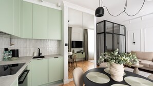 A modern kitchen with light green cabinets, a black countertop, and a dining area with a round table and chairs. - Plac Politechniki Pistachio Apartment (Warszawa)