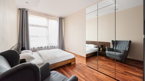 A modern hotel room with a large bed, a seating area with a chair, a small table, and a mirror wall.