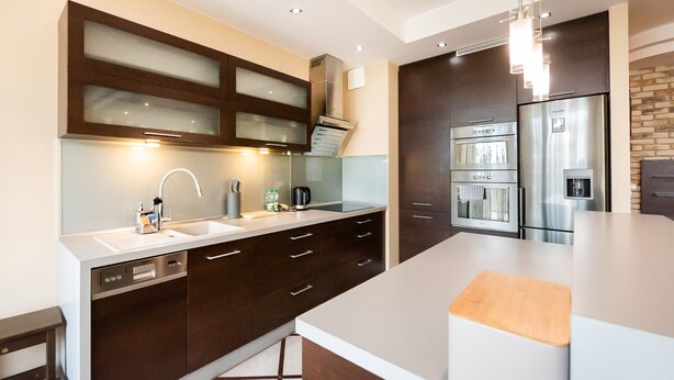A modern kitchen with dark cabinetry, stainless steel appliances, and a white countertop.