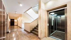 A modern hotel lobby with a marble floor, a staircase, and an elevator.