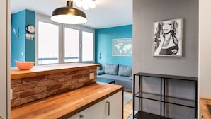 A modern kitchen with a wooden countertop, a hanging light fixture, and a view to a living area with a blue wall and a world map. - Ratusz Arsenał Modern City Apartment (Warszawa)