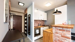 A compact kitchen with a brick accent wall, white cabinets, and a wooden countertop. - Ratusz Arsenał Modern City Apartment (Warszawa)