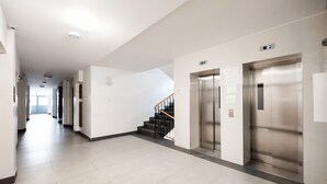 A modern hallway with two elevators, a staircase, and a clean, tiled floor. - Ratusz Arsenał Modern City Apartment (Warszawa)
