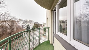 A balcony with a green railing, a window, and a view of a street with buildings and trees. - Praga-Południe Czechowicka Apartment (Warszawa)