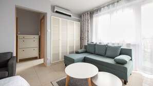 A modern living room with a grey sofa, a white coffee table, and a grey armchair. There is a wardrobe with a mirror and a door leading to another room. An air conditioning unit is mounted on the wall. - Praga-Południe Czechowicka Apartment (Warszawa)