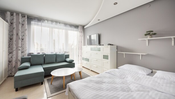 A modern bedroom with a bed, a sofa, a TV, and a dresser. - Praga-Południe Czechowicka Apartment (Warszawa)
