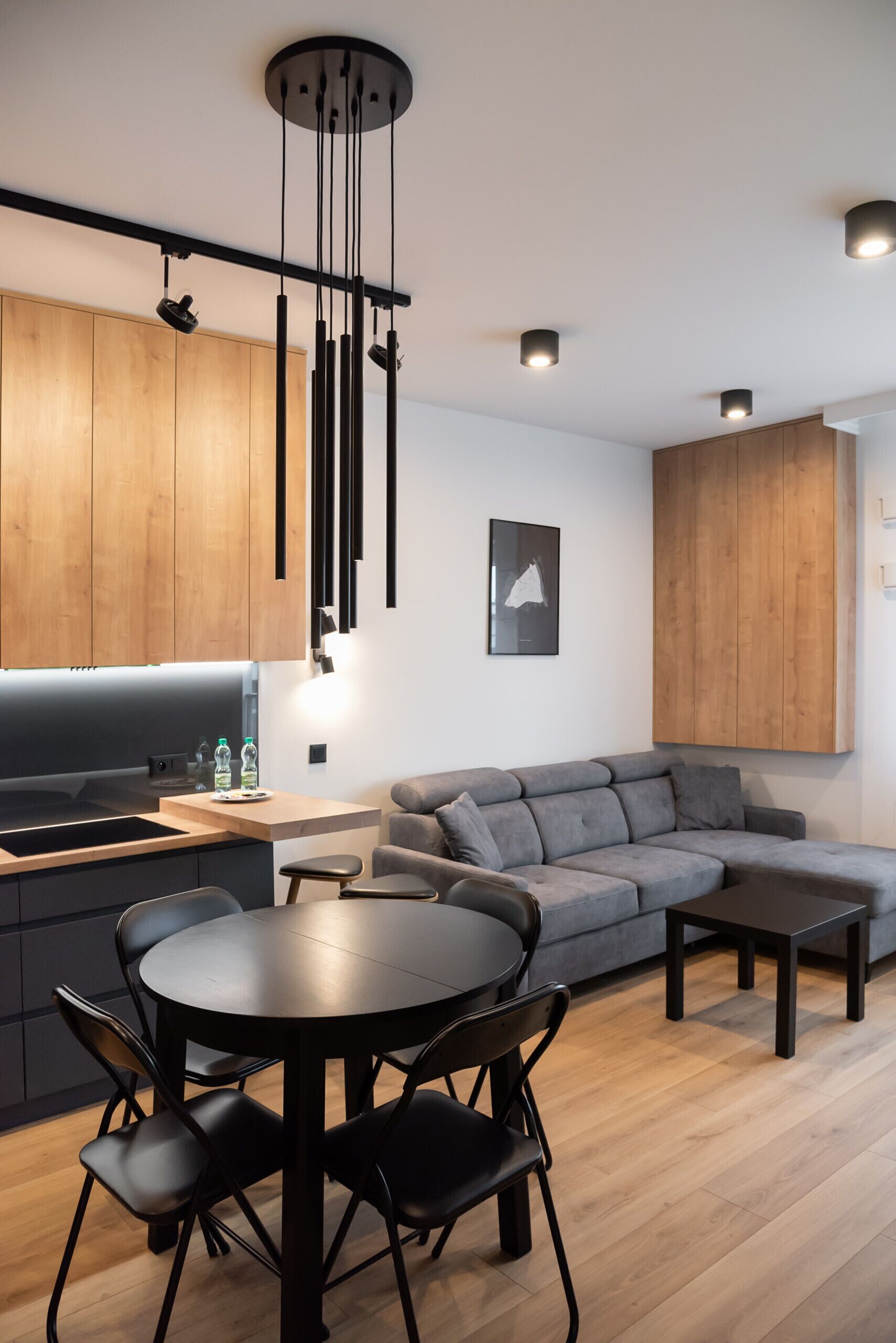Una cocina moderna con armarios de madera, un comedor con una mesa redonda y sillas, y un sofá seccional gris.