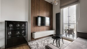 Un salon moderne doté d’un grand téléviseur à écran plat fixé à un mur en bois, d’une vitrine contenant des verres à vin, d’un canapé confortable et d’un coin repas avec une table et des chaises.