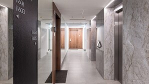 A modern hallway with numbered doors, a wooden door at the end, and an elevator on the right. - New Varsovia Comfort 1604 (Warszawa)