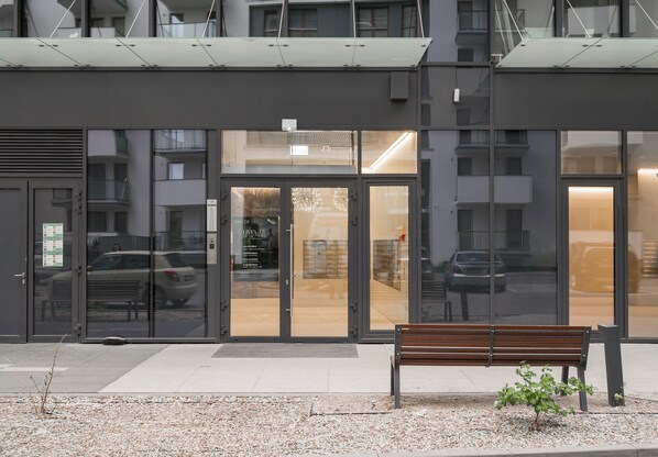 A building entrance with glass doors, a bench, and a small plant. - New Varsovia Comfort 1604 (Warszawa)