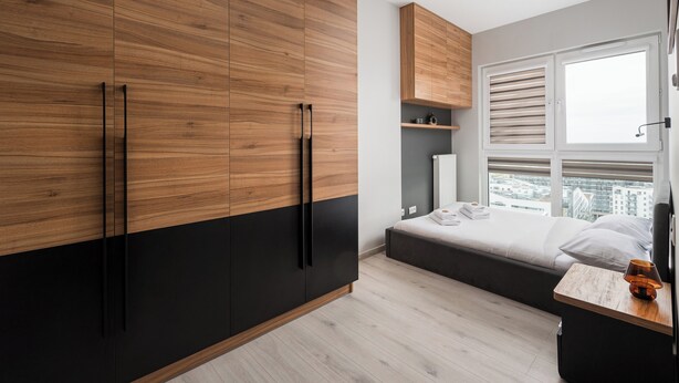 A modern bedroom with a bed, wooden wardrobe, and a small table with a lamp. - New Varsovia Comfort 1604 (Warszawa)