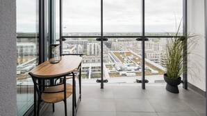 A balcony with a wooden table and chairs, a potted plant, and a city view through large windows. - New Varsovia Comfort 1604 (Warszawa)