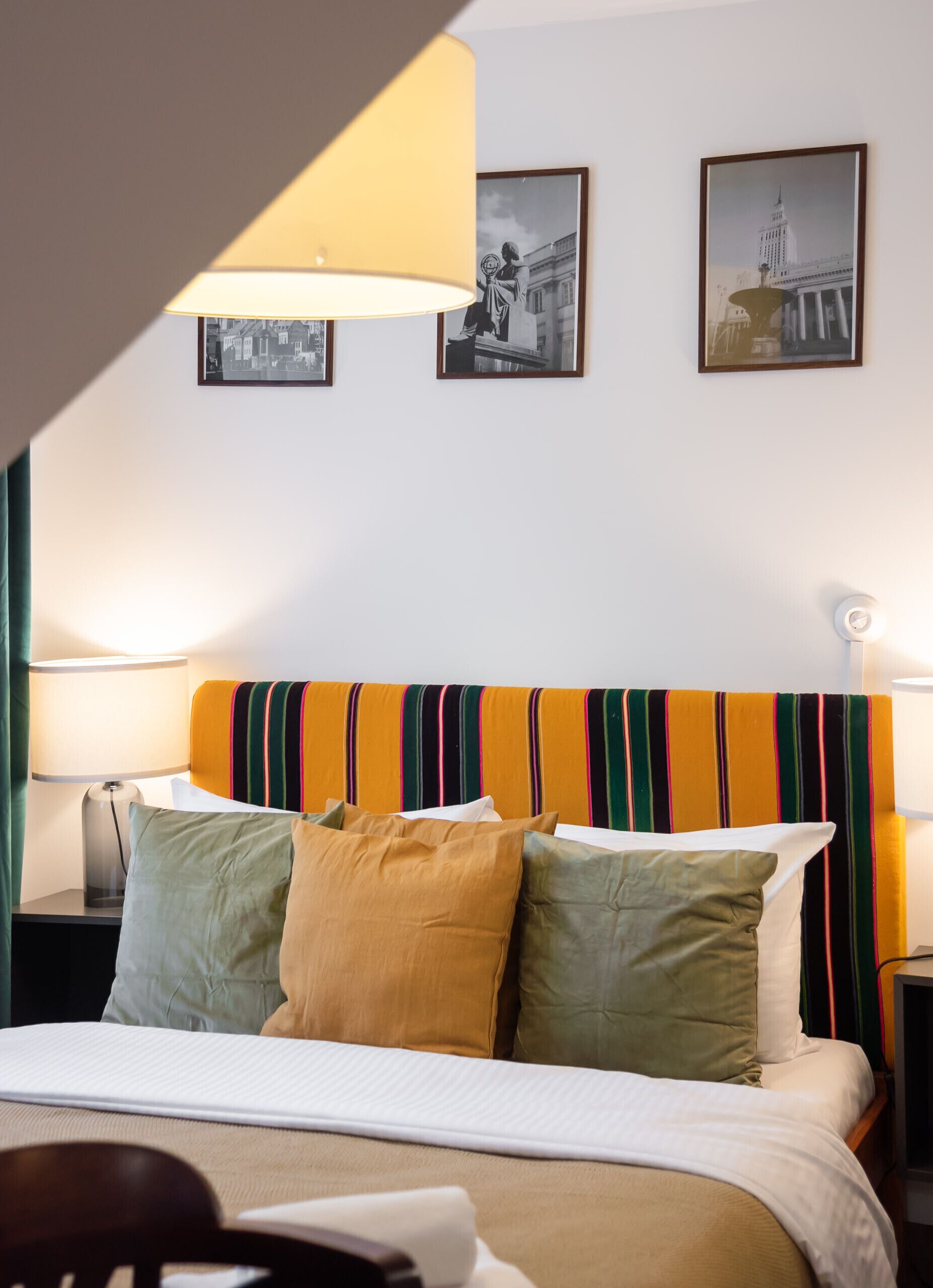 Ein Hotelzimmer mit einem Bett, zwei Nachttischlampen, einem gestreiften Kopfteil und zwei gerahmten Bildern an der Wand.