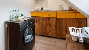 Une cuisine compacte équipée d’un lave-linge, de meubles en bois et d’un coin repas avec des chaises en plastique.