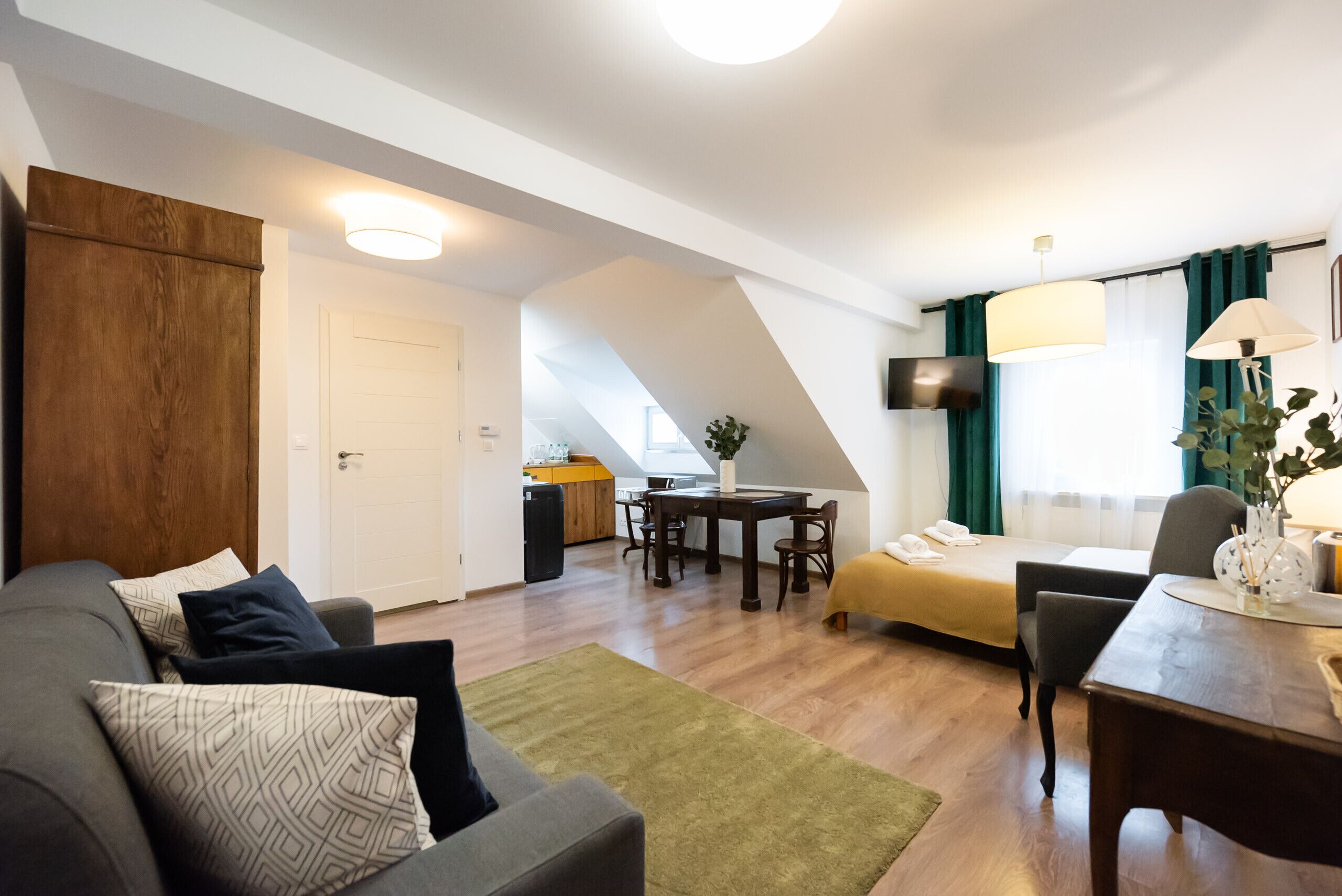 A modern hotel room with a sofa, a dining table, a bed, and a TV.