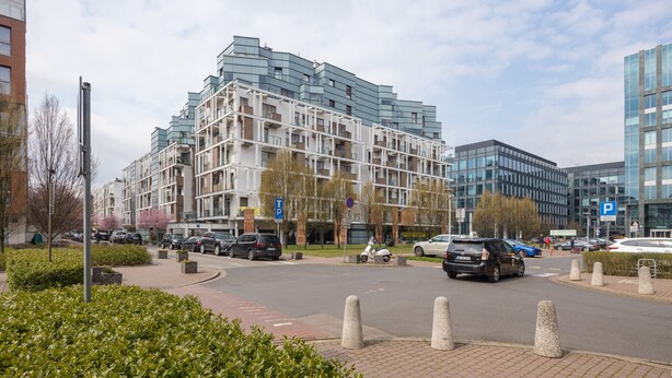 Een moderne straat in de stad met meerlaags woongebouwen, een zebrapad en een parkeerplaats.