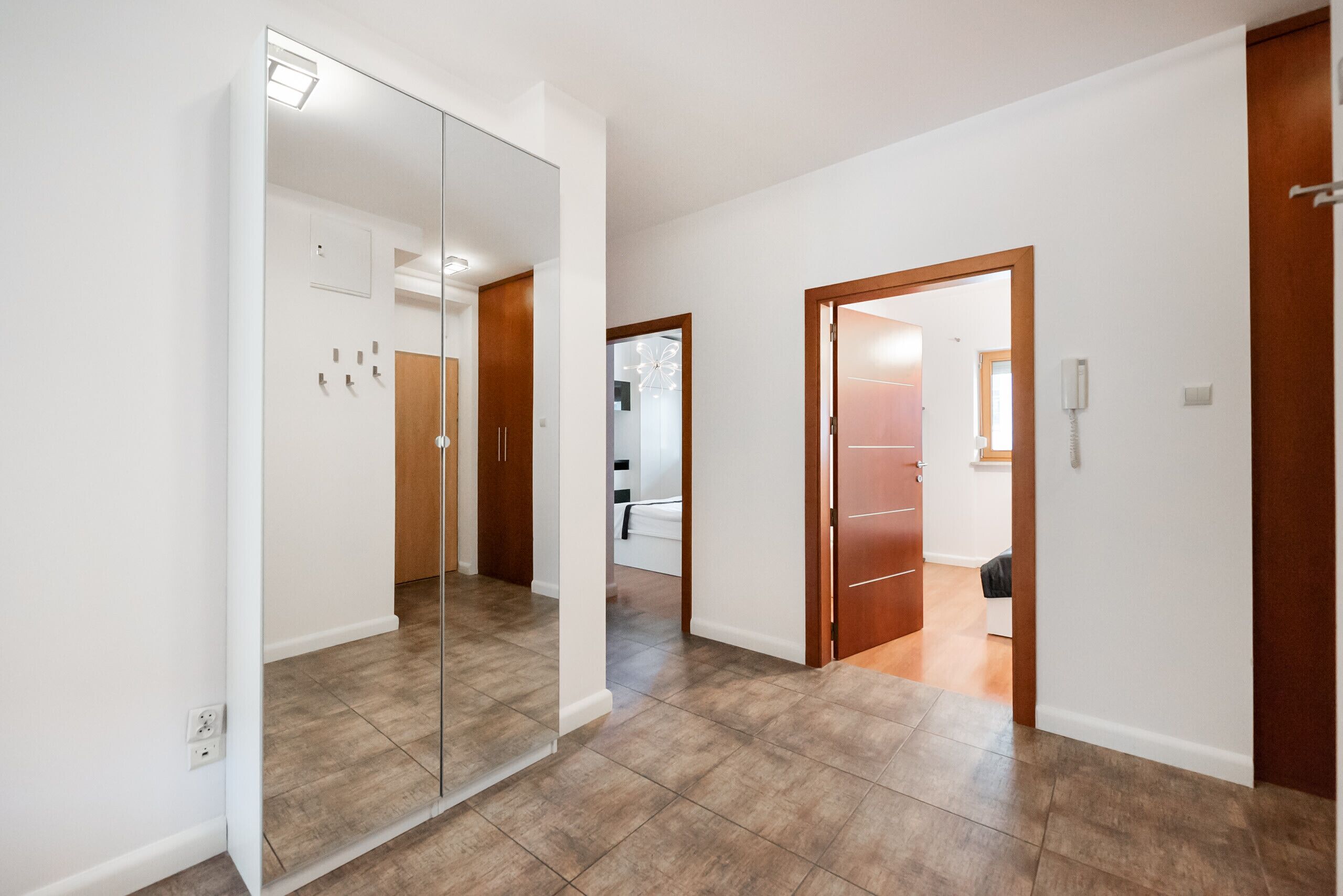 Ein Flur mit einem Spiegelkleiderschrank, Holztüren und einem gefliesten Boden.