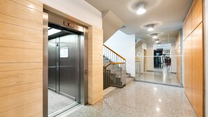 Moderni hissi, jossa on digitaalinen näyttö, puuseinät, kiillotettu lattia ja metallikaiteella varustetut portaat.