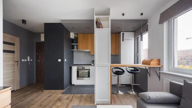 A modern kitchen with white cabinets, a built-in oven, and a dining area with a bar stool. - Arte Praga Koneser Apartment (Warszawa)