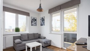 A modern living room with a grey sofa, a white coffee table, and large windows offering a view of the city. - Arte Praga Koneser Apartment (Warszawa)