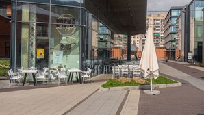 An outdoor seating area with tables and chairs in front of a modern building with glass windows. - Arte Praga Koneser Apartment (Warszawa)
