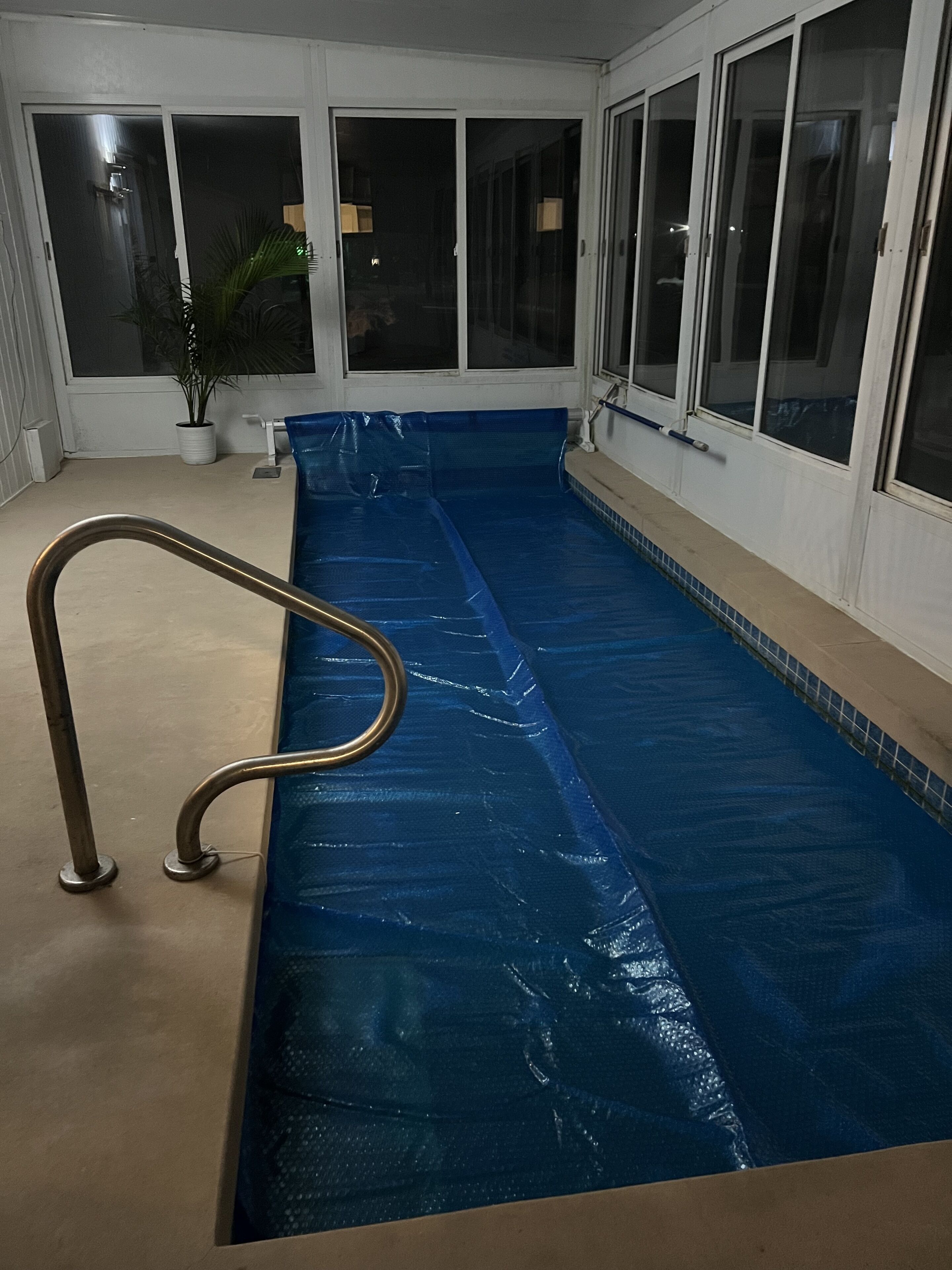 A swimming pool with a blue cover, a metal handrail, and a potted plant.