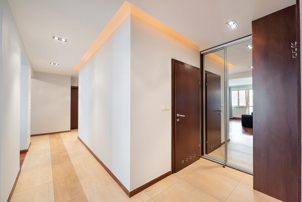 A hallway with a wooden floor, white walls, and a sliding glass door leading to a room.