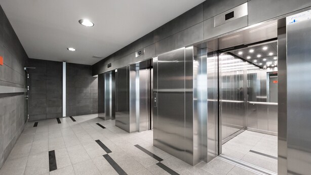 Un espace moderne pour les ascenseurs, avec des portes métalliques et un sol carrelé.