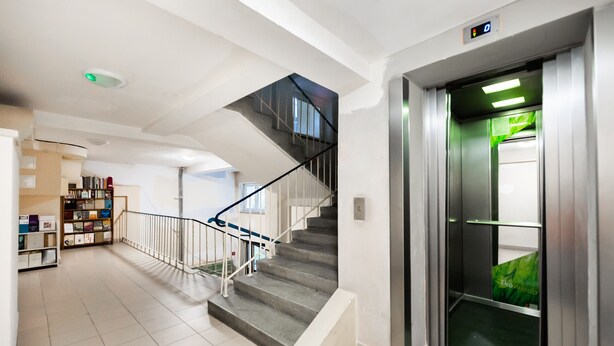 A modern interior with a staircase, an elevator, and a bookshelf with various items.