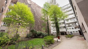 A courtyard with a brick wall, a tree with pink flowers, and a building with multiple balconies.