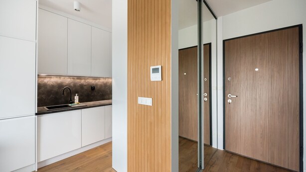 Une cuisine moderne avec des armoires blanches, un mur d’accent en bois et une porte en verre donnant sur une pièce.
