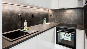 Une cuisine moderne avec des armoires blanches, un comptoir noir, un dosseret en acier inoxydable, un four encastré et un lave-vaisselle.