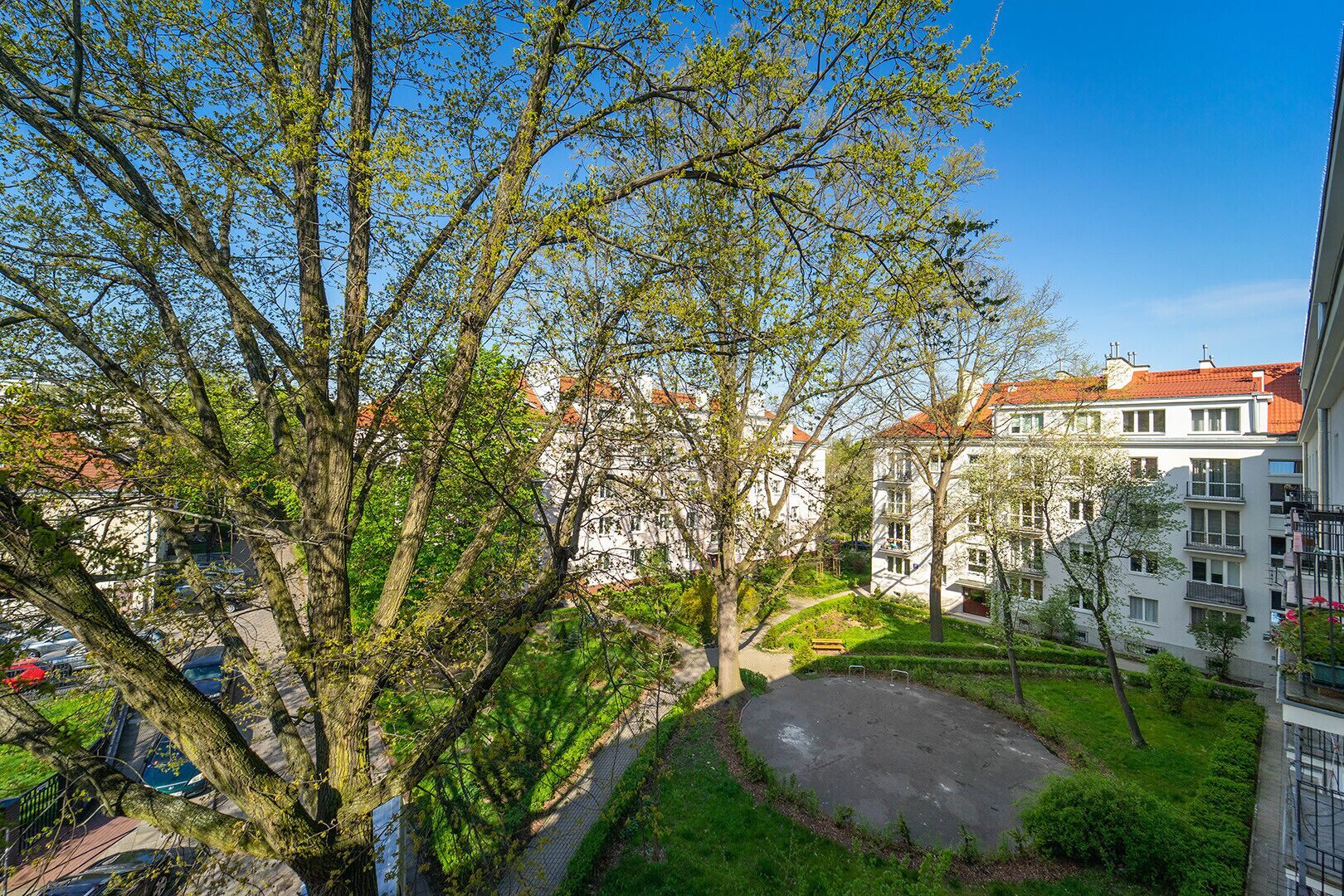Un cortile con un pavimento lastricato, circondato da alberi e edifici con tetti in tegole rosse.