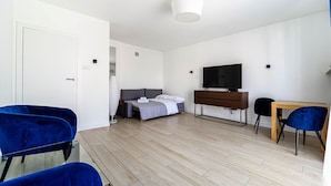 A modern hotel room with a bed, a TV, a wooden desk, and two blue chairs.