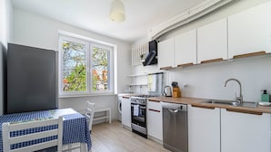 A compact kitchen with a dining area, a washing machine, a dishwasher, and a window with a view of trees.