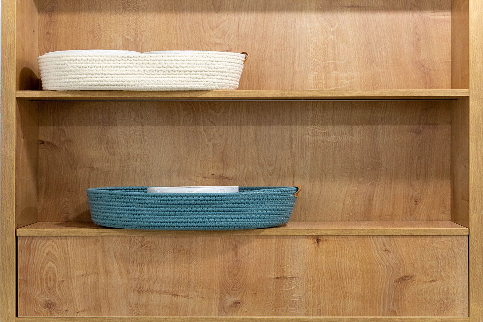 A wooden shelf unit with two storage baskets, one white and one blue, on separate shelves.
