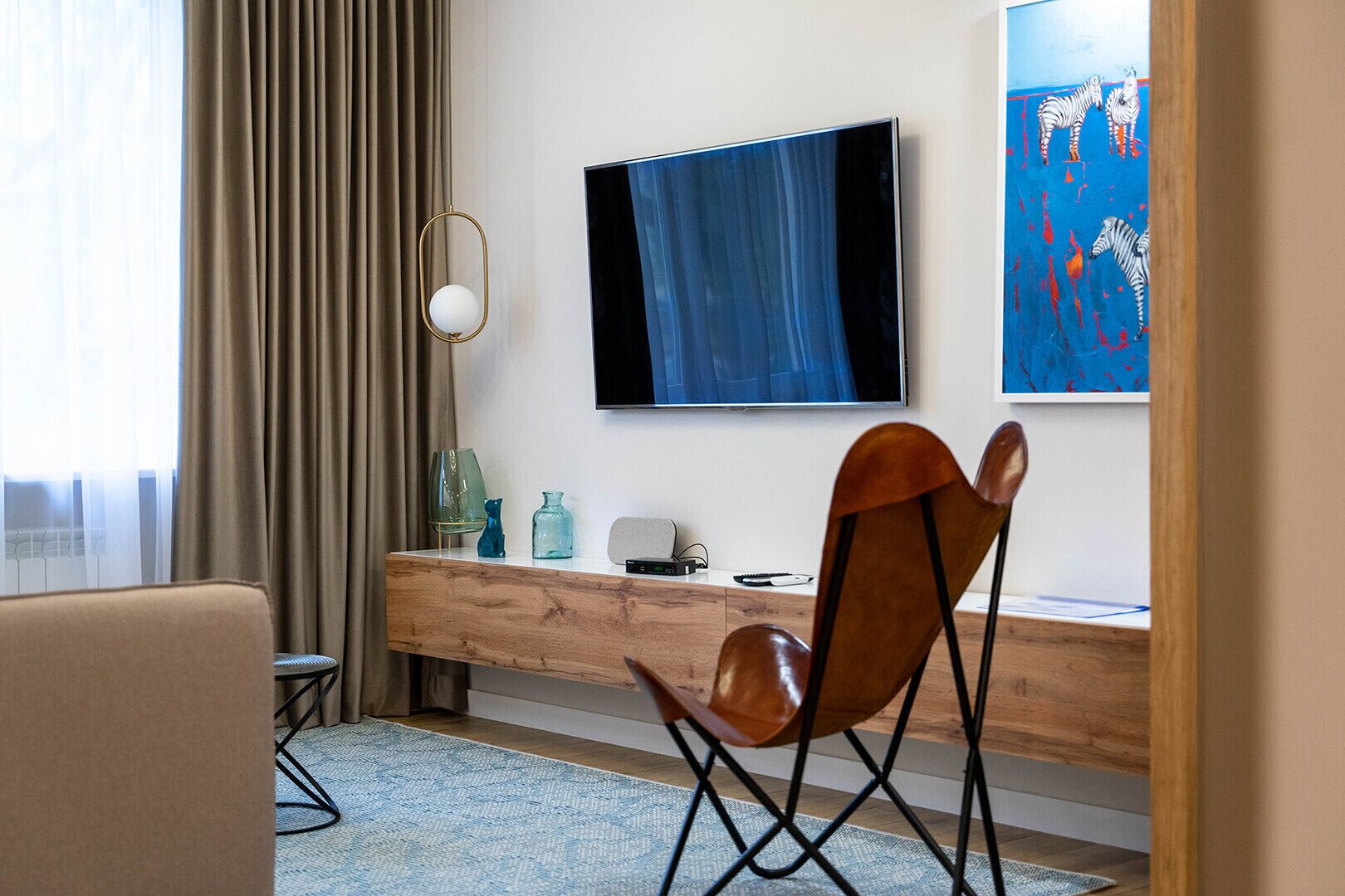 Una habitación de hotel moderna con un escritorio de madera, un televisor montado en la pared y un cuadro con cebras.