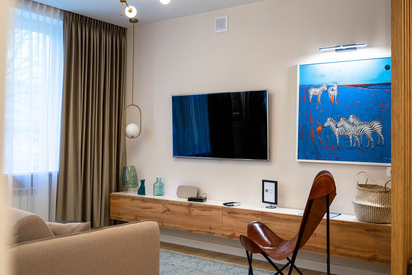 Un salon moderne doté d’un grand téléviseur à écran plat, d’une console en bois, d’un fauteuil en cuir et d’un tableau représentant des zèbres.