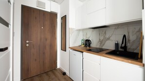A compact kitchen with white cabinets, a wooden door, a marble backsplash, a black sink, and a small white refrigerator. - New Varsovia Comfort 346 (Warszawa)