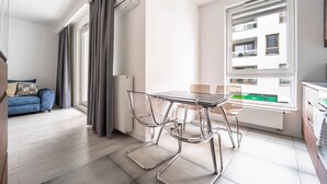 A modern apartment with a dining area, a sofa, and a view of a building through large windows.