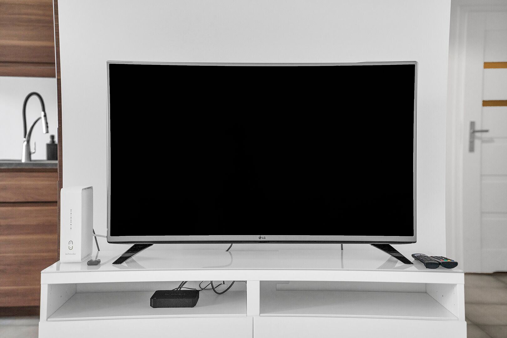A flat-screen TV on a white entertainment center with a remote control and a power strip.