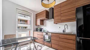 A modern kitchen with wooden cabinets, a black refrigerator, a built-in oven, and a glass dining table.