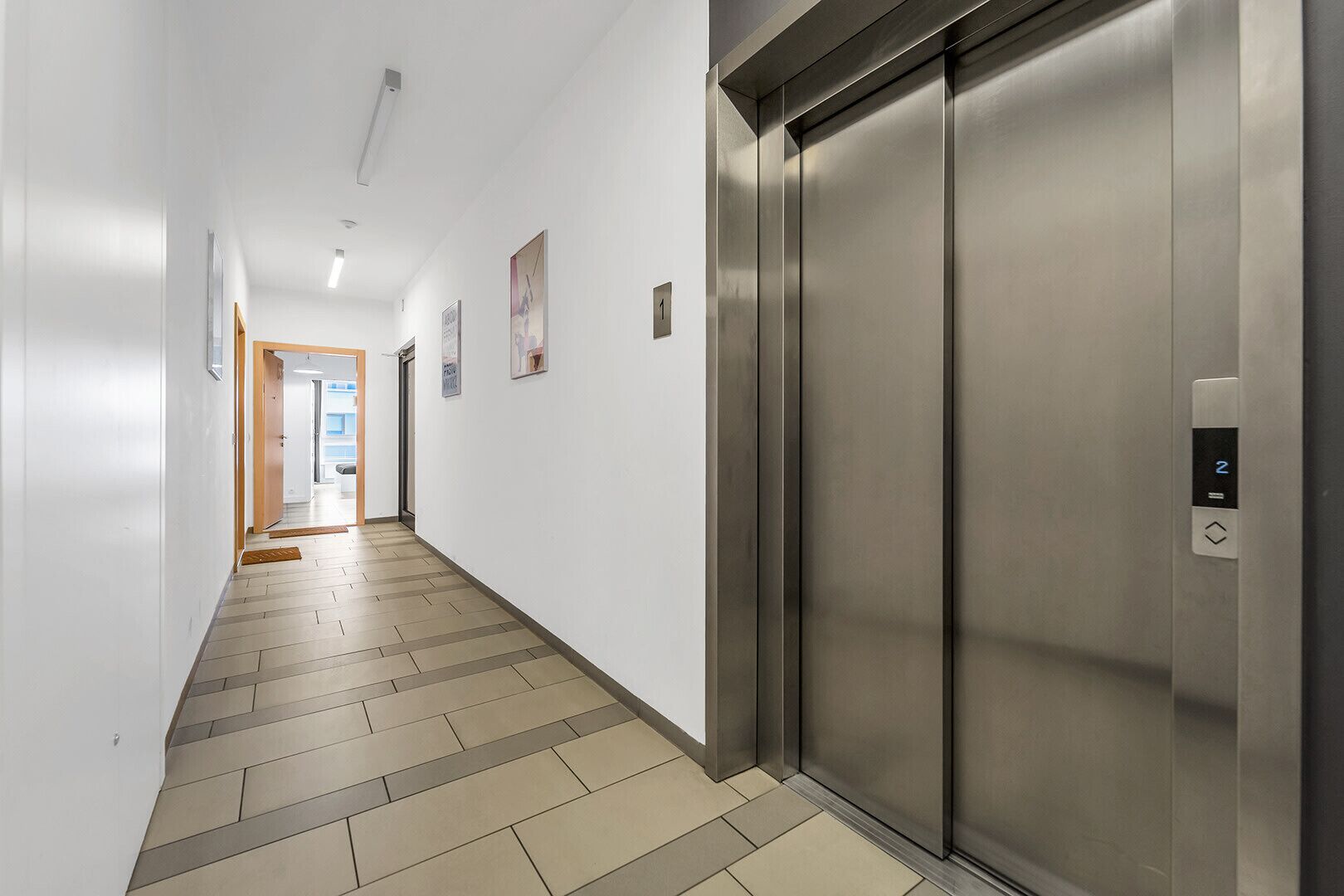 A modern elevator with a digital display, a hallway with tiled flooring, and a door leading to another room.