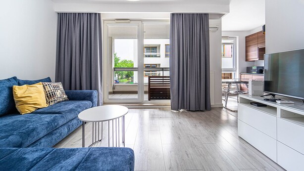 A modern apartment with a blue sofa, a small round table, a TV, and a kitchen area.
