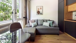 Ein modernes Wohnzimmer mit einem grauen Ecksofa, einem Glastisch und Blick auf Bäume durch große Fenster.