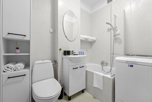 Bathroom features a white toilet, sink, shower, and bathtub, with shelves for towels and amenities.