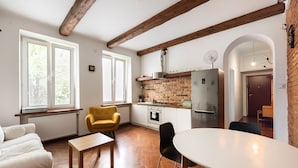 Una cocina moderna con ladrillo visto, vigas de madera, un comedor con mesa y sillas blancas, y un sillón amarillo.
