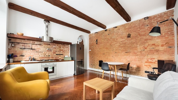 Una cocina moderna con paredes de ladrillo visto, vigas de madera y una zona de comedor con mesa y sillas.