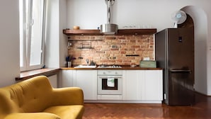 Una cocina con pared de ladrillo, vigas de madera, refrigerador de acero inoxidable y una silla amarilla.