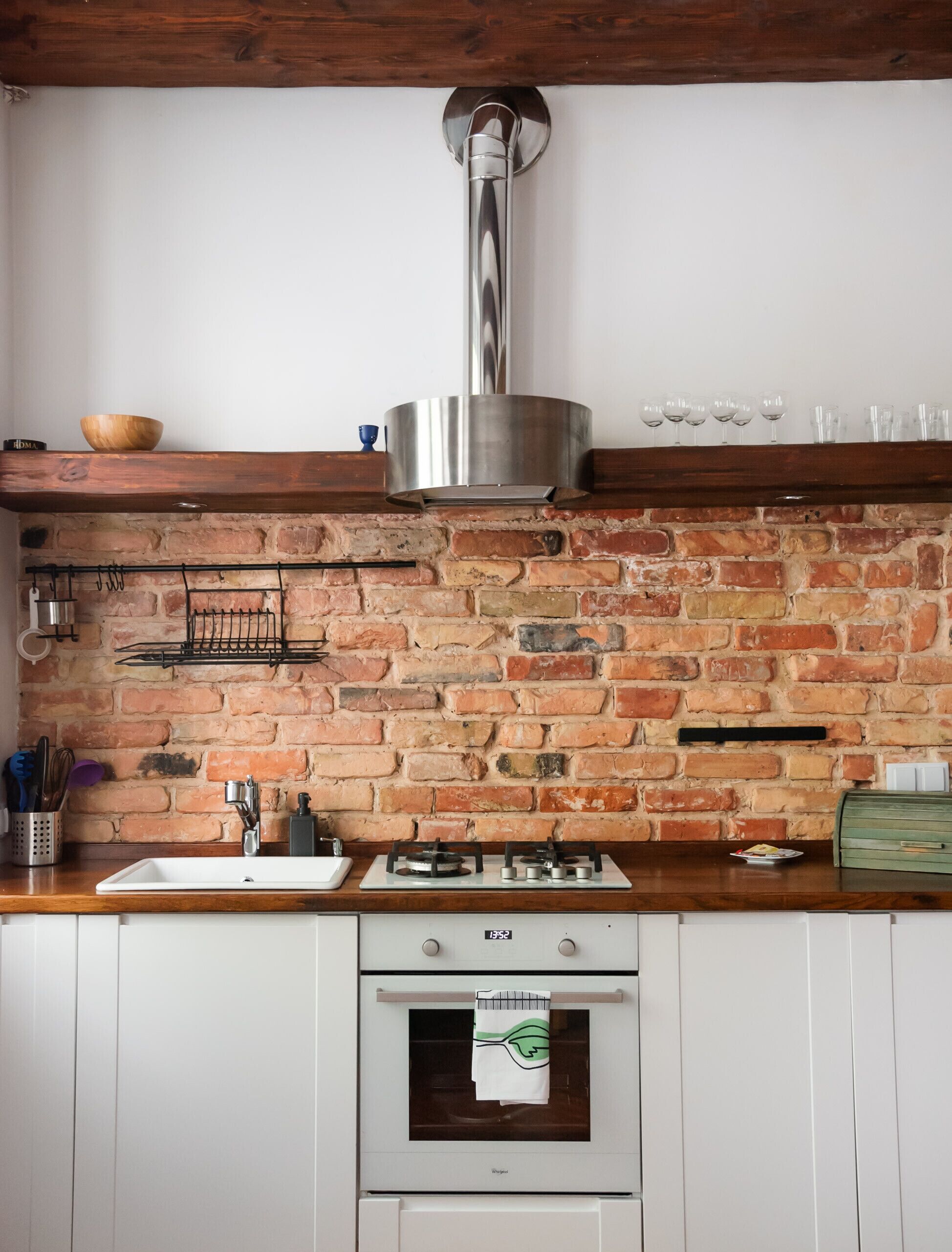 A kitchen with a brick wall, wooden countertop, stainless steel range hood, and a white oven.
